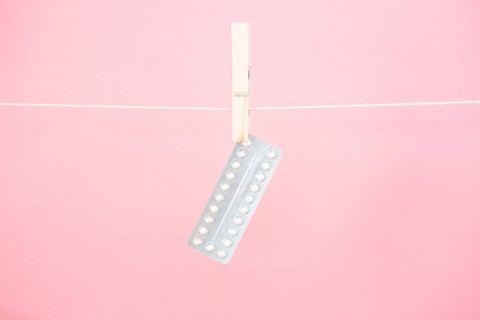 Contraceptive pill blister pack hanging from line on pink background