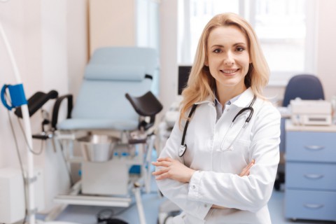 Full of joyful emotions at work. Positive delighted qualified gynecologist standing in the gynecology cabinet while expressing positivity and enjoying working responsibilities