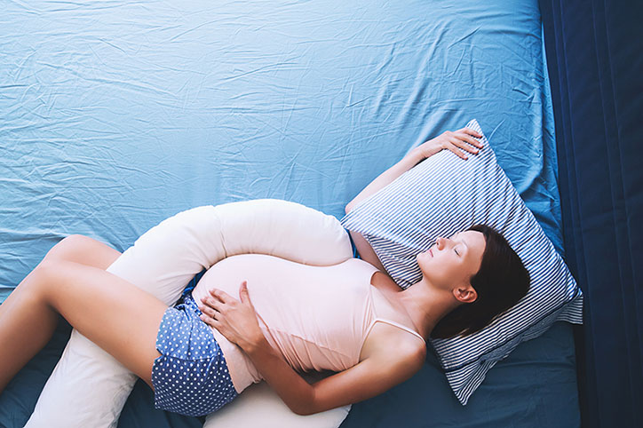 Beautiful pregnant woman relaxing or sleeping with tummy supporting pillow at bed.